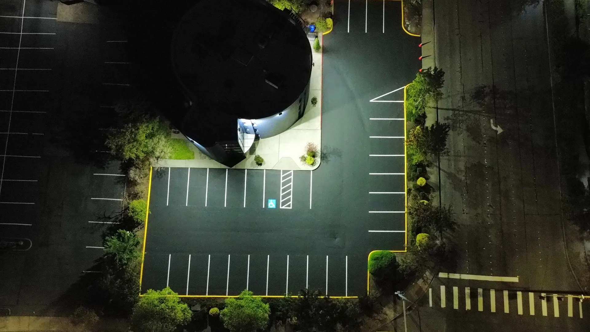 Overhead drone view of a complete parking lot restripe around a commercial building at night
